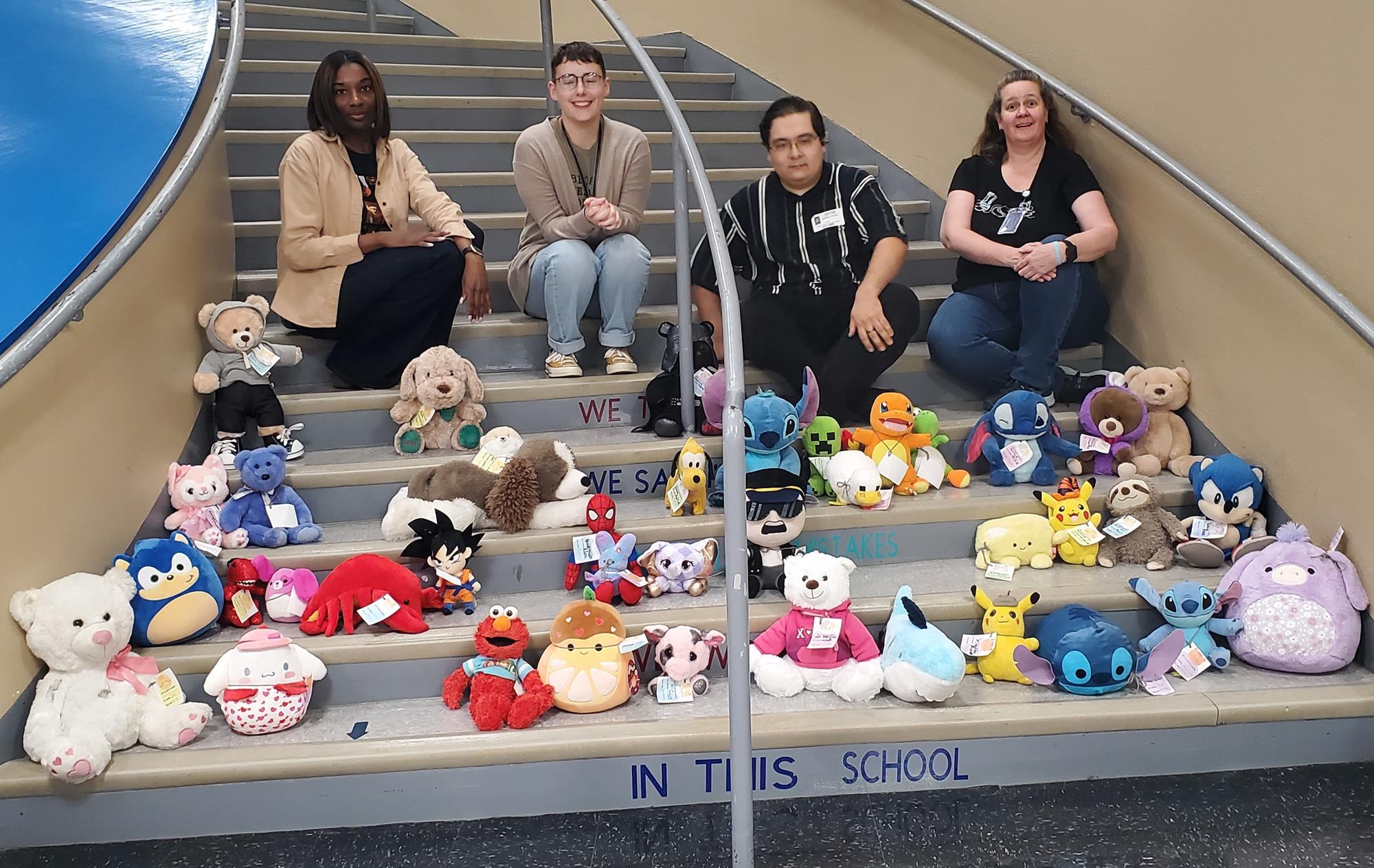 Ms. Gordon, Ms. Wells, Mr. Kocian, Ms. White on stairs with stuffed animals